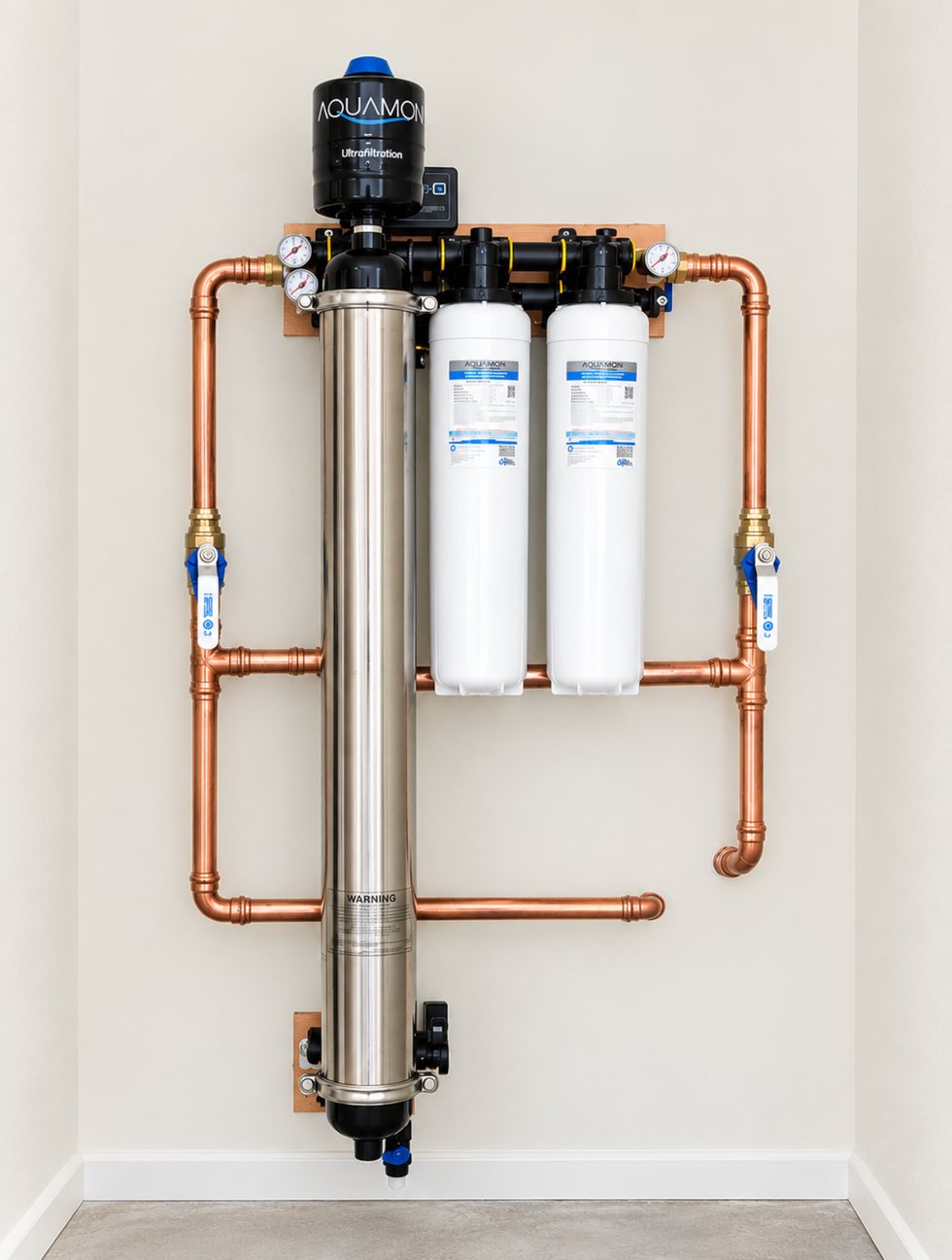 An Aquamor ultrafiltration system wall-mounted in a utility alcove — stainless membrane vessel, twin carbon post-filter cartridges, pressure gauges and copper pipework